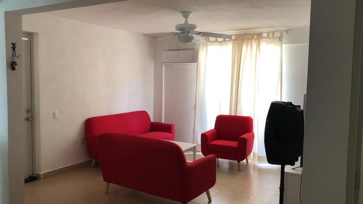 Sala del departamento con sillones rojos y cortinas claras